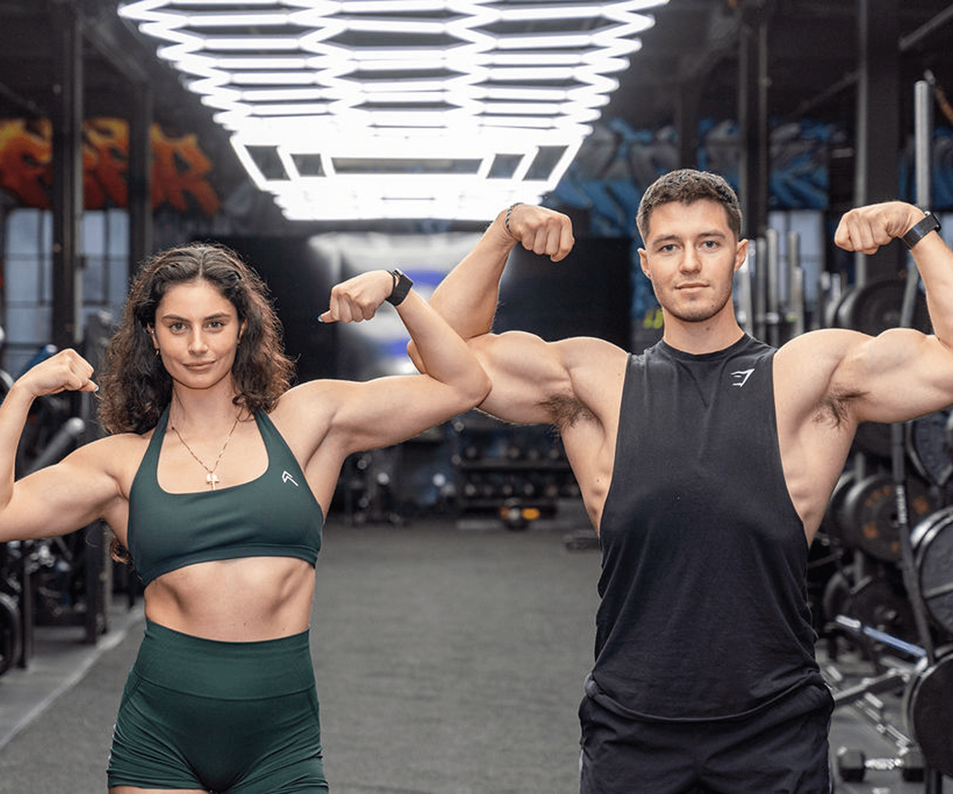 Two fit individuals flexing their muscles in a gym setting.